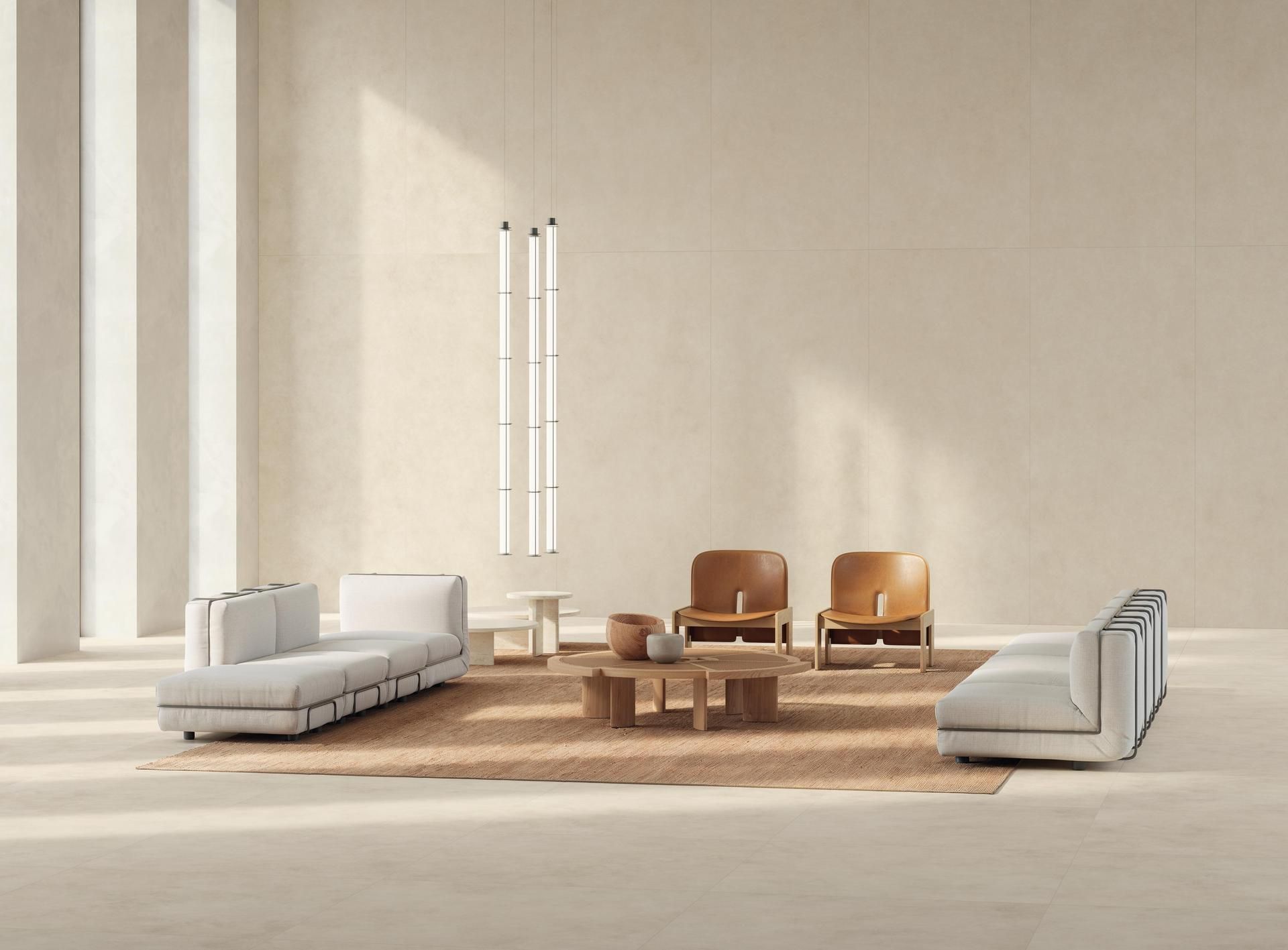 Salon minimaliste avec murs beiges, canapés blancs, tables en bois et deux fauteuils sous de hautes suspensions.