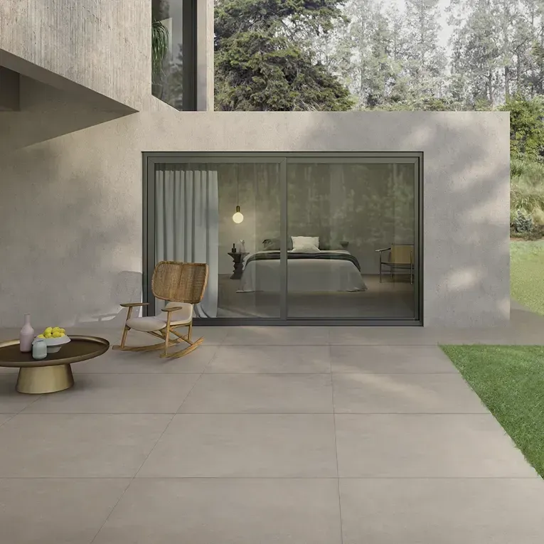 Terrasse moderne en béton avec portes coulissantes en verre, chaise en bois, table basse et une chambre visible à l'intérieur