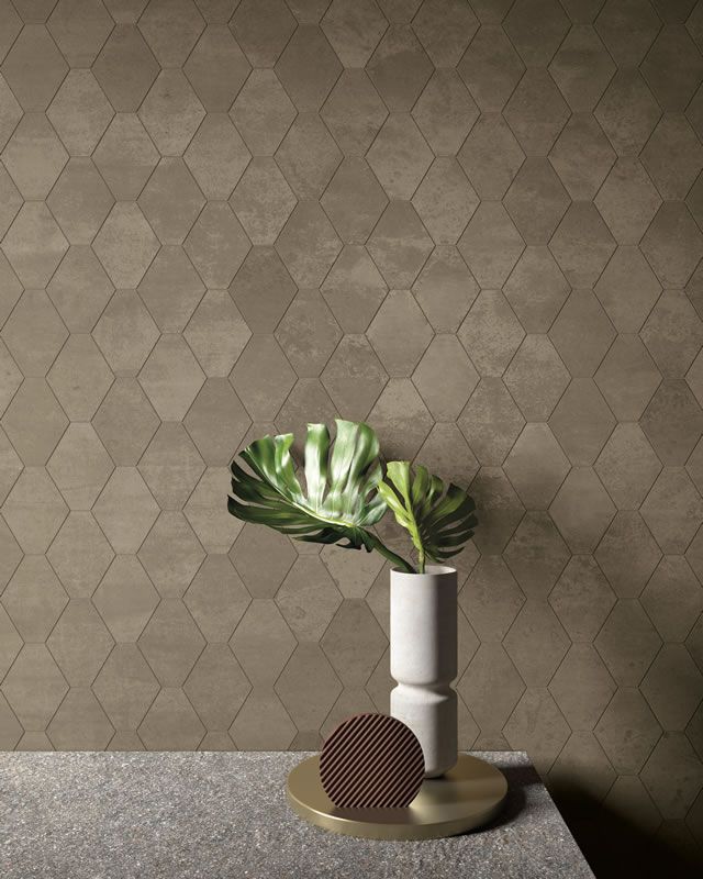 Vase minimaliste avec une feuille verte sur des cylindres blancs empilés, devant un mur texturé.