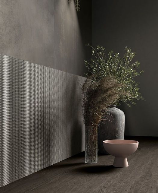 Intérieur minimaliste avec un vase de branches séchées, un grand cylindre et un bol rose sur un sol sombre.
