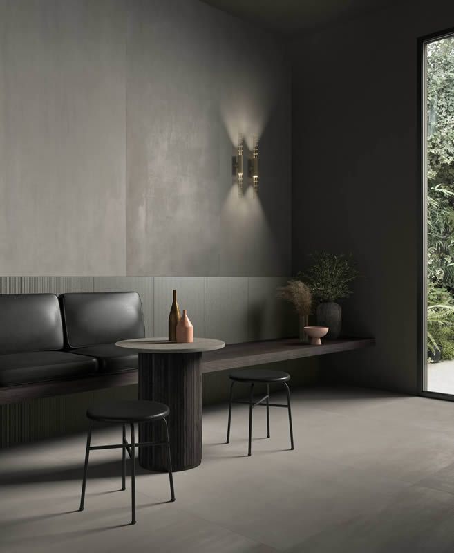 Coin repas moderne et minimaliste avec chaises noires, table ronde, murs gris et porte ouverte sur un espace vert.