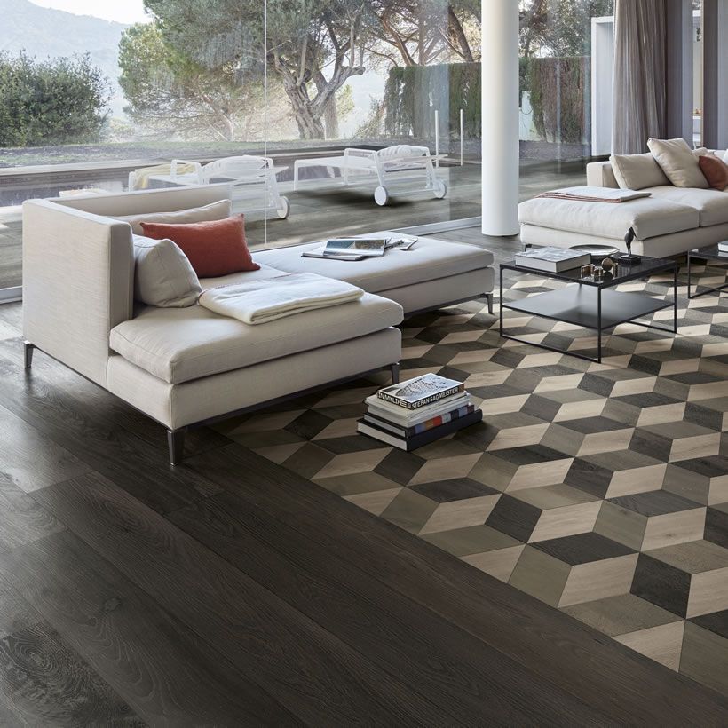 Salon moderne avec canapés beiges, tapis géométrique et grandes fenêtres donnant sur une terrasse
