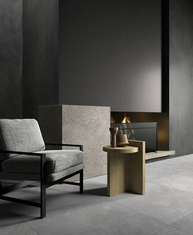 Salon minimaliste moderne avec fauteuil gris, blocs de pierre et petite table d'appoint en bois près d'une cheminée.