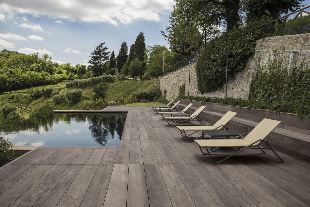 Terrasse moderne en bois avec chaises longues au bord d'une piscine et d'un jardin luxuriant