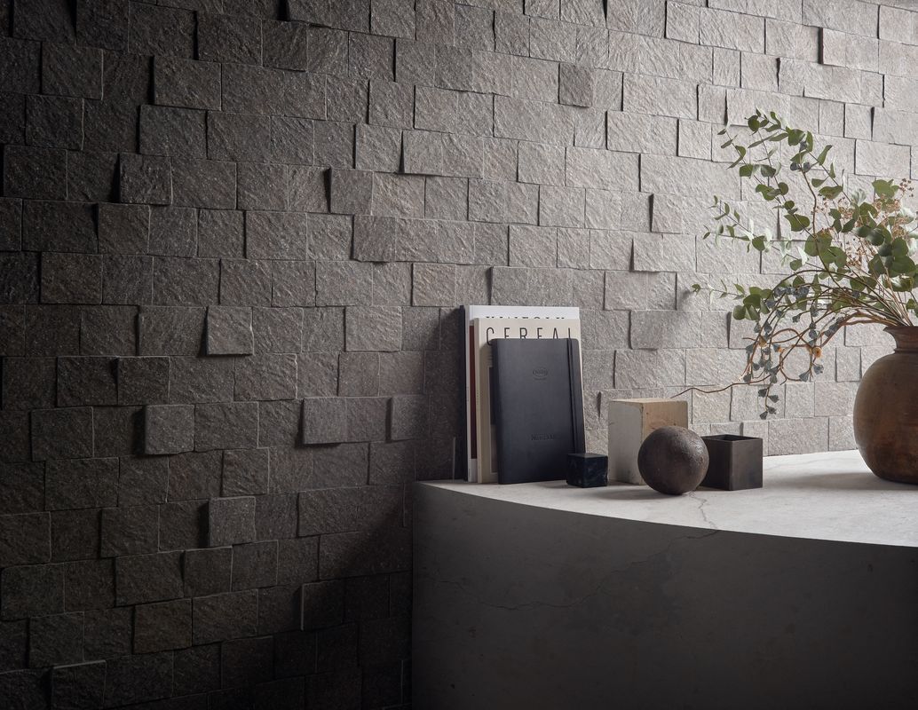Étagère minimaliste avec un petit appareil sombre, un vase en bois et une plante, le tout sur un mur noir texturé.