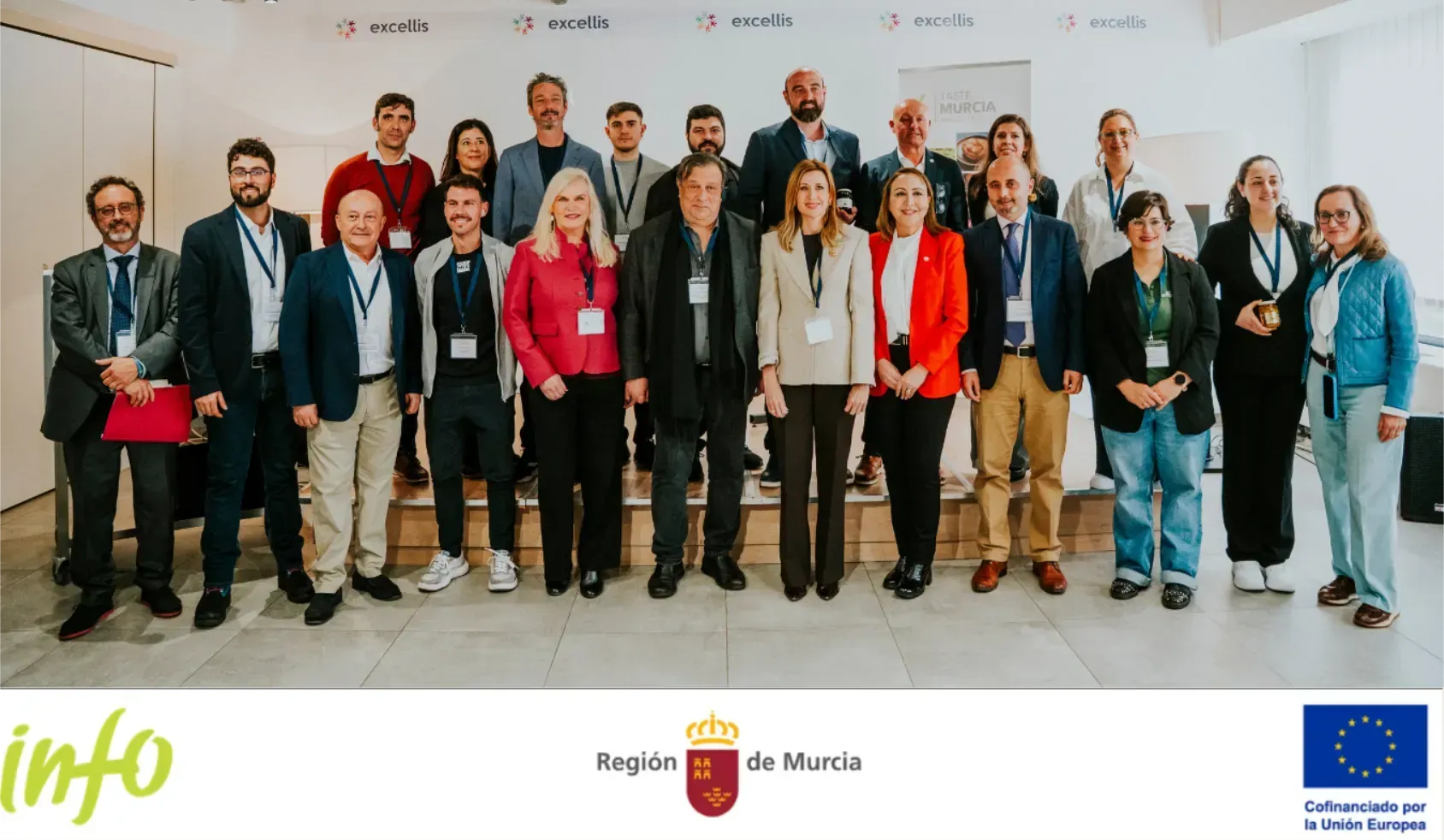 Grupo de personas posando en el interior de un evento formal, con logotipos y pancartas en la parte inferior.