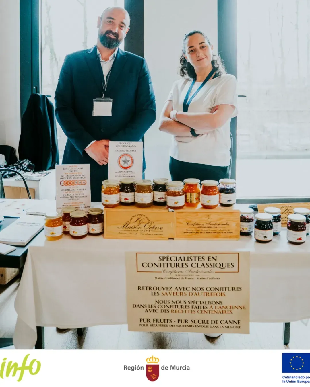 Exhibición en un stand con frascos de miel y certificados sobre una mesa en un espacio interior luminoso.