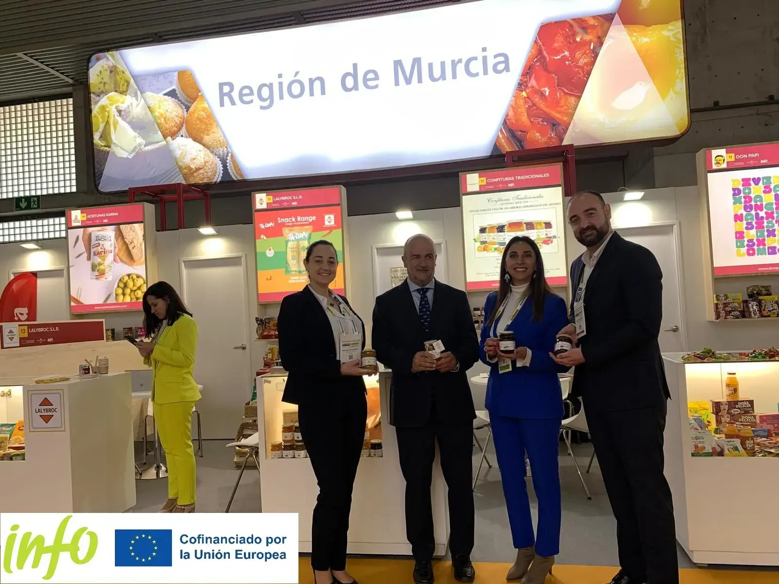 Cinco personas posan en un stand de la Región de Murcia, decorado con coloridos expositores y folletos.
