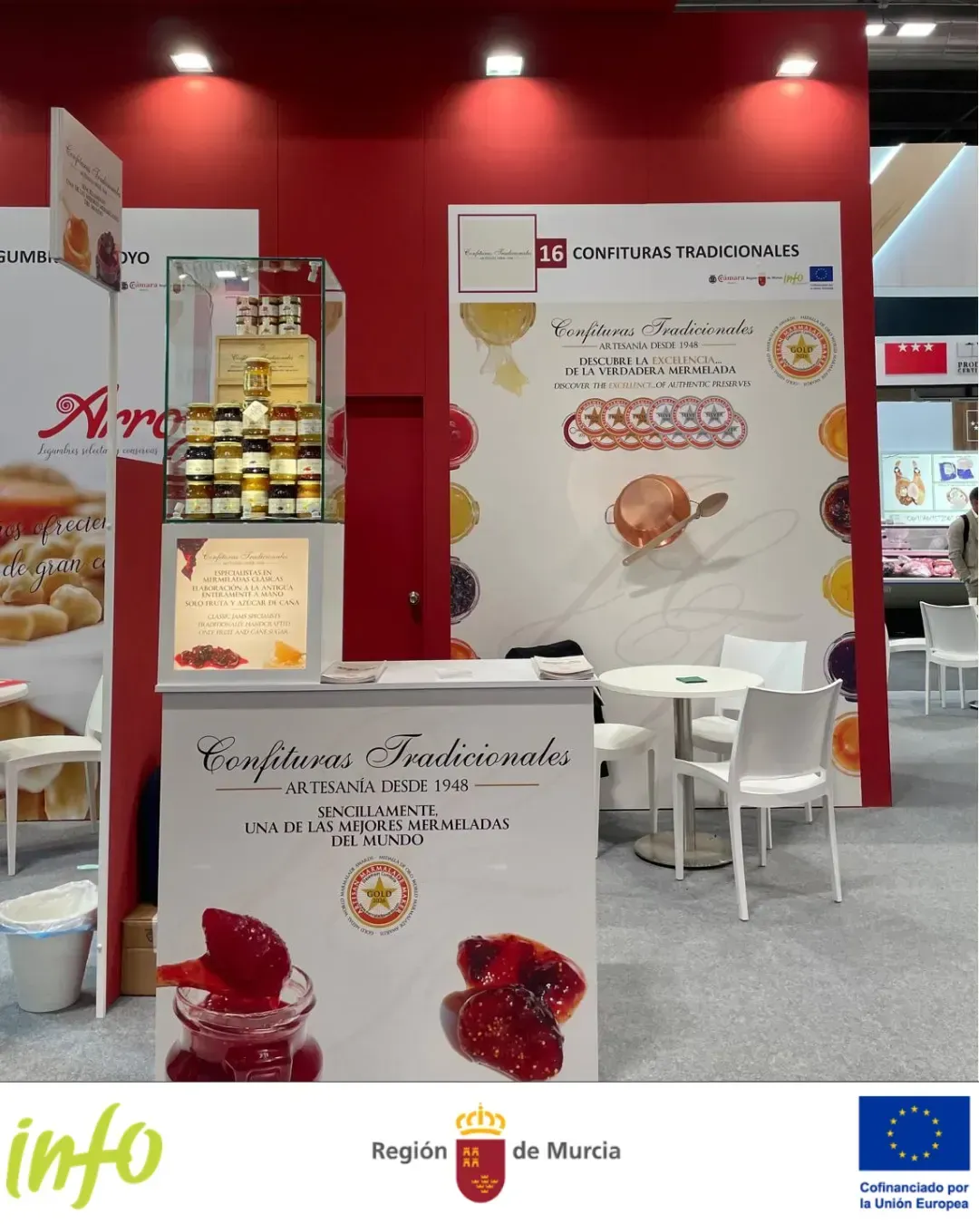 Stand rojo para feria comercial con expositores de productos, mesas y pancartas de marca.