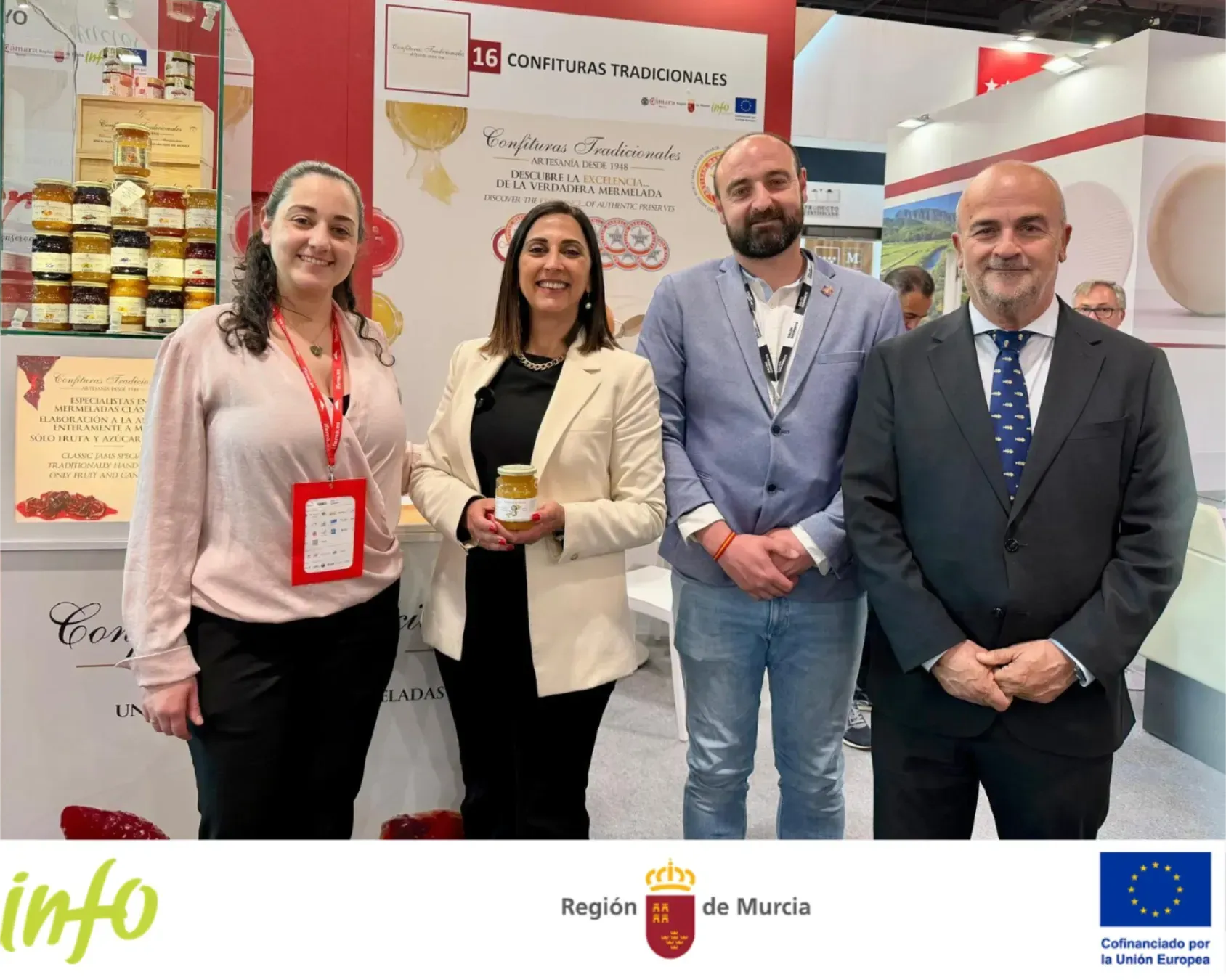 Cuatro personas posando en un stand de feria, sonriendo frente a paneles de exhibición de marcas y estantes de productos.