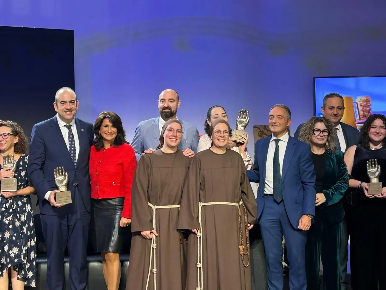 Un grupo de personas en el escenario sosteniendo premios, con dos oradores ataviados con togas en el centro