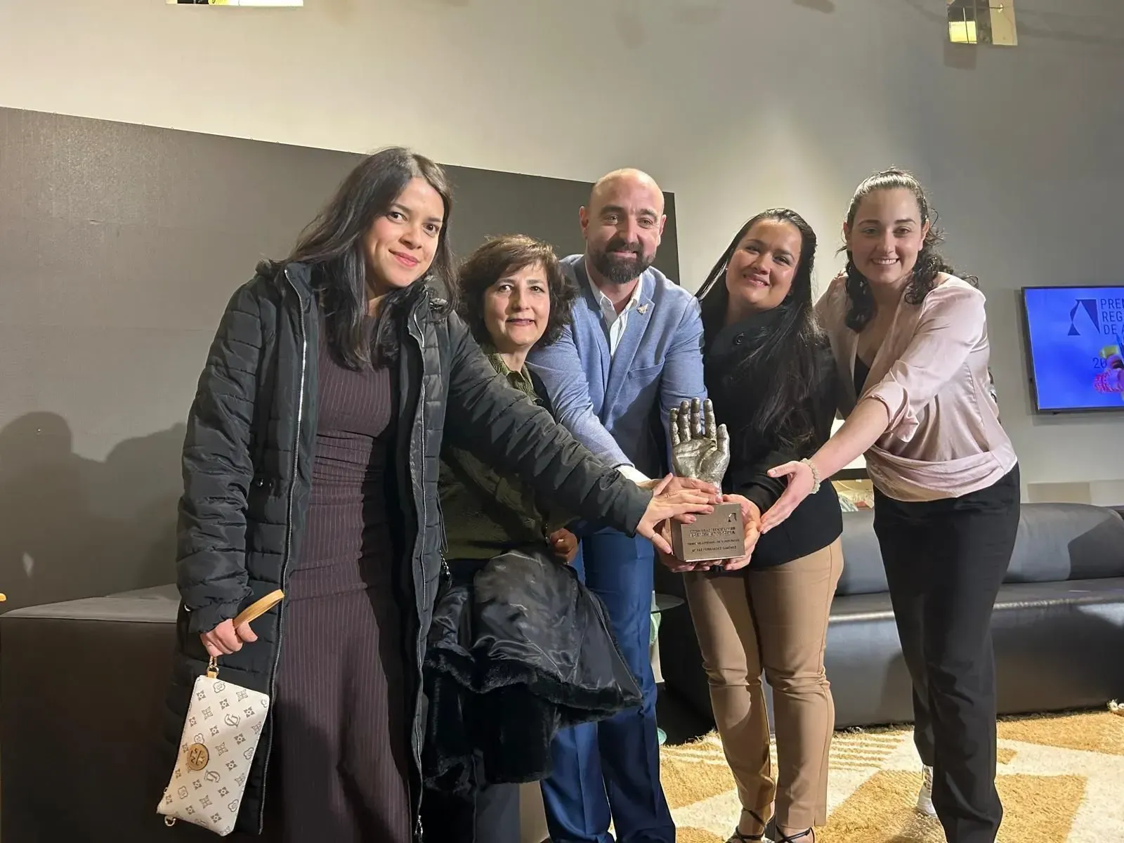 Cinco personas sonriendo y juntando las manos en una habitación que parece una oficina.