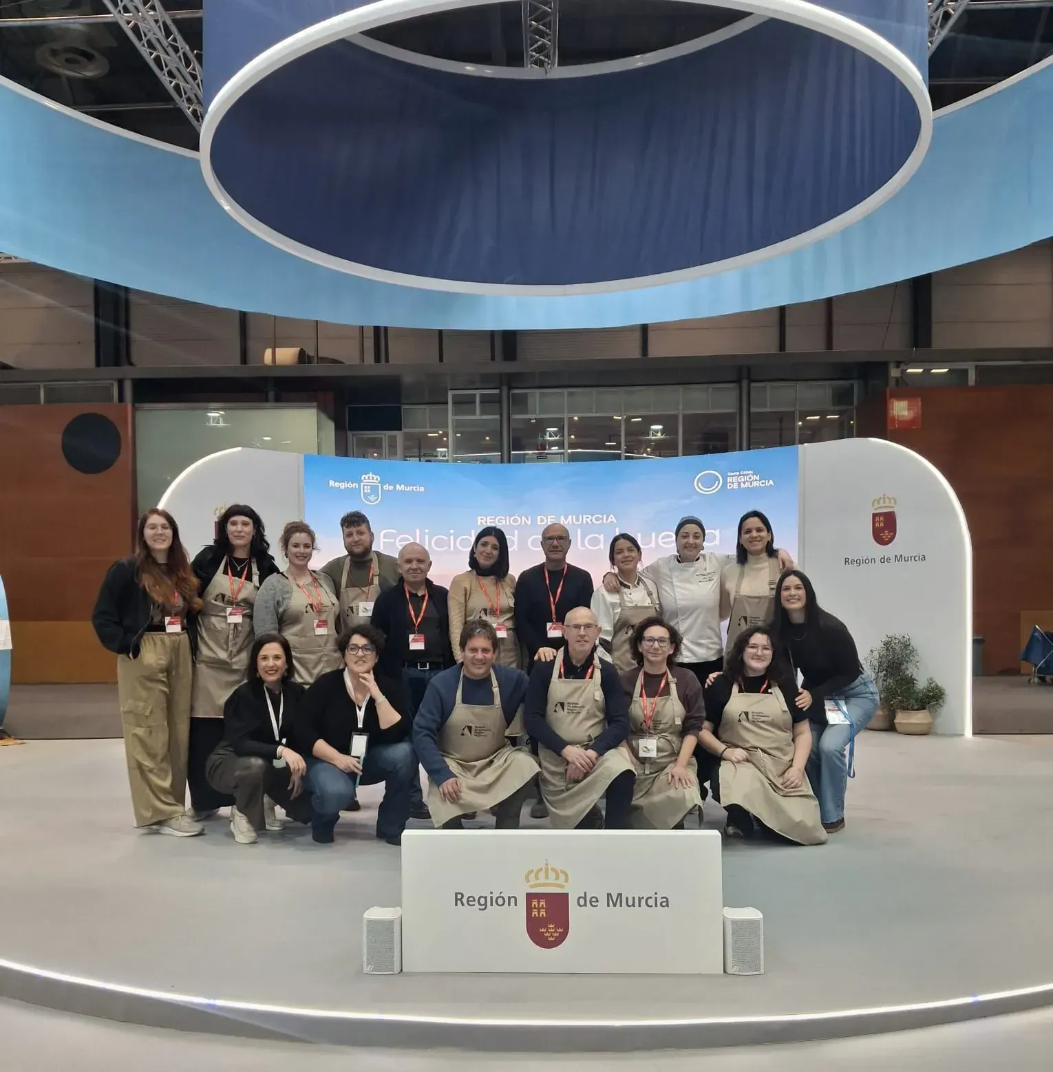 Grupo de personas posando en el interior de un evento formal, frente a un fondo azul y el emblema de la ciudad.