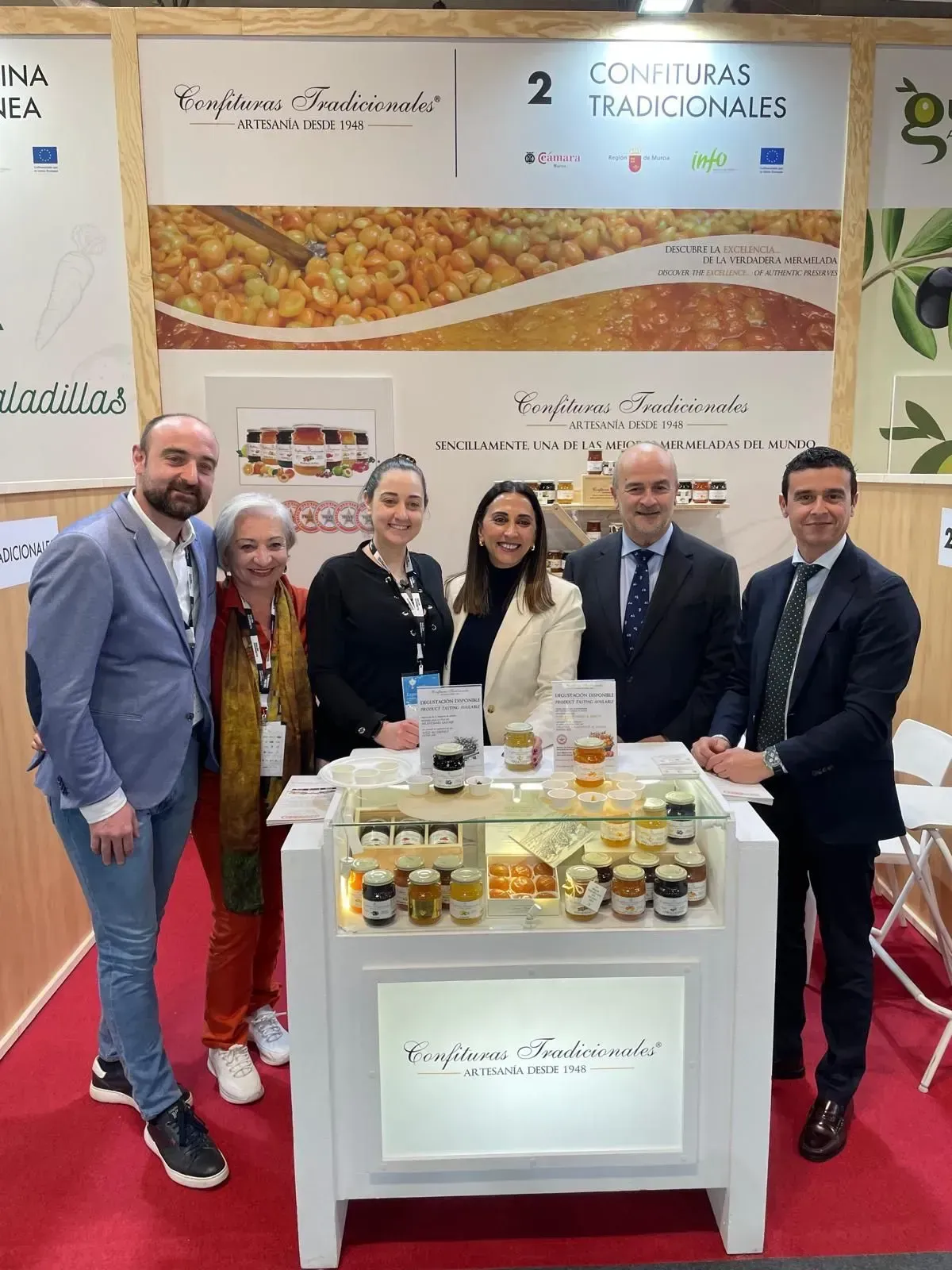 Cinco personas con traje posando en un stand comercial con exhibiciones de comida y un fondo de marca.
