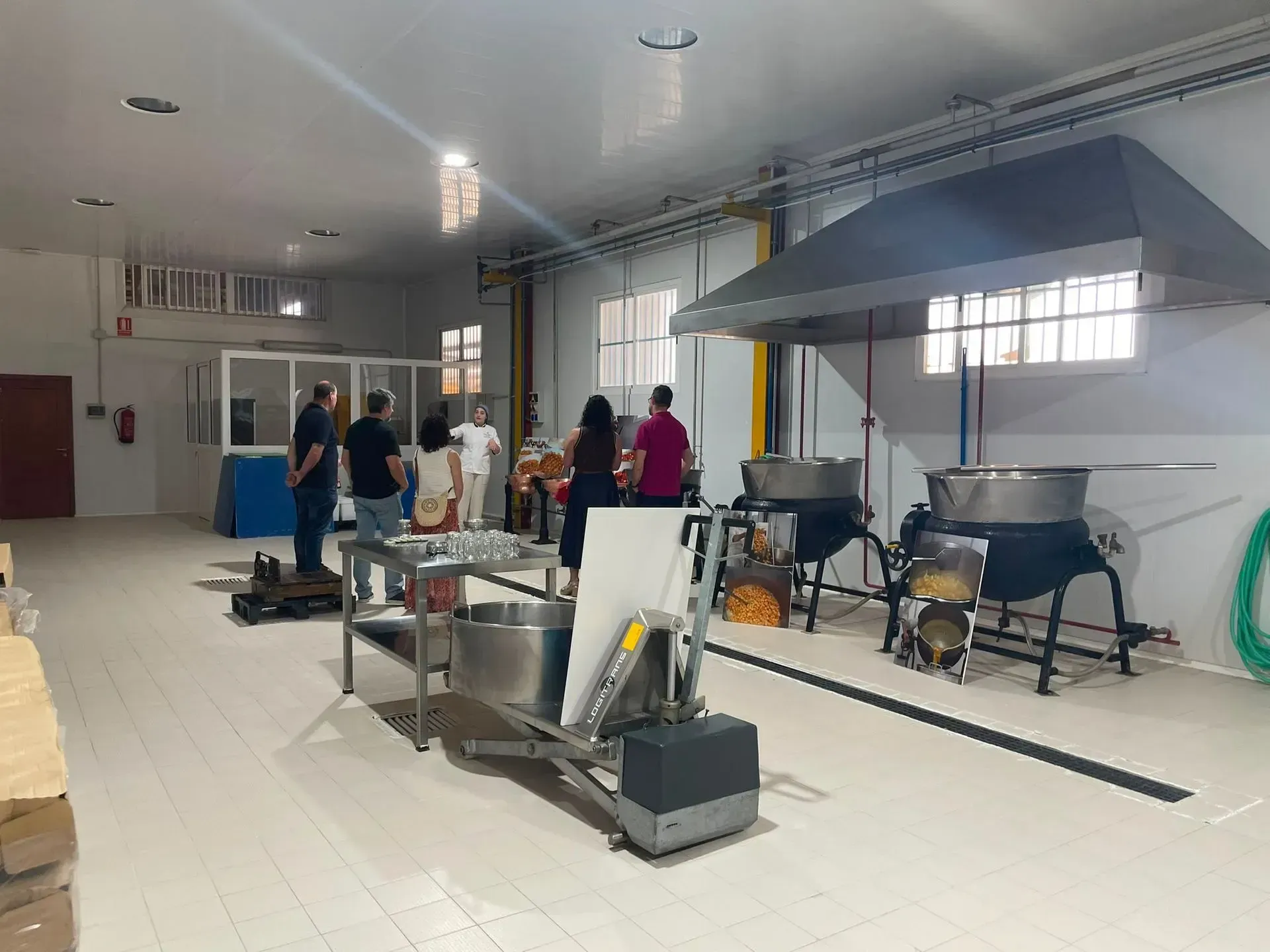 Taller industrial con personas de pie cerca de equipos y maquinaria metálica en una habitación luminosa.