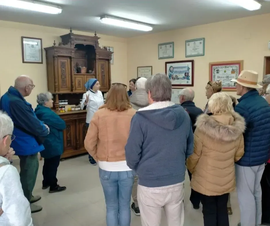 Un grupo de personas recorre una sala con un altar o armario de madera, mientras escuchan a un guía.