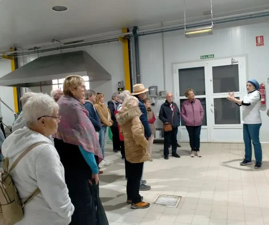 Grupo de personas escuchando a un guía en una habitación interior con azulejos, una gran campana extractora