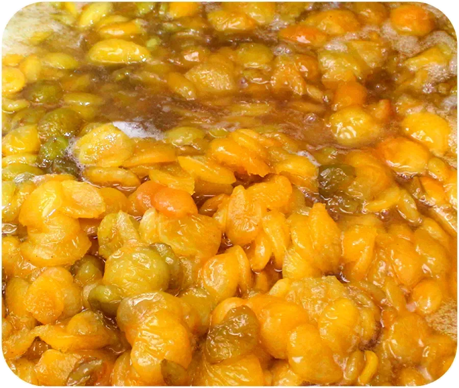 Primer plano de trozos de fruta de color naranja amarillento brillante cociéndose a fuego lento en almíbar.