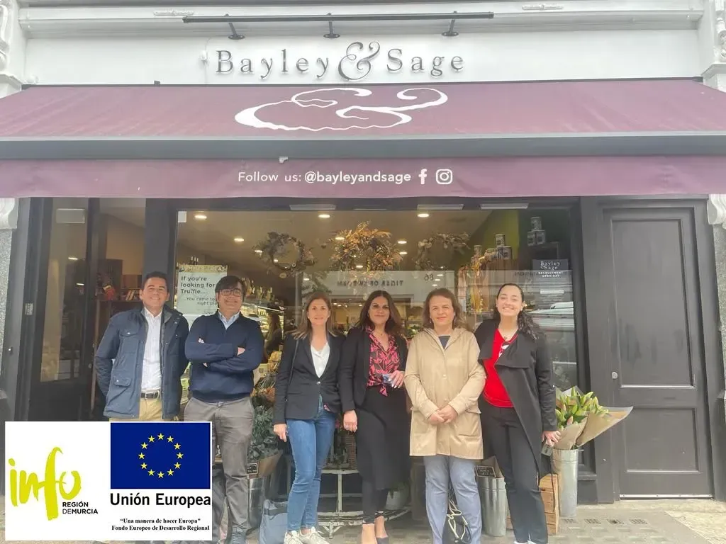 Cinco personas permanecen de pie frente a la entrada de la tienda Bayley & Sage, bajo un toldo color burdeos.