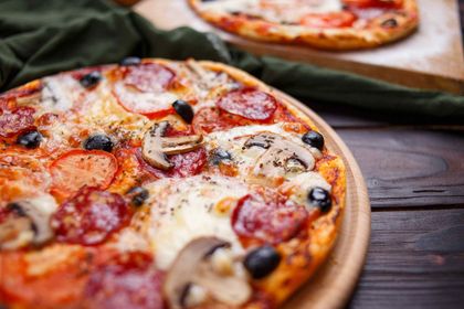 Pizza de pepperoni y champiñones sobre una tabla de madera. Otra pizza borrosa al fondo.
