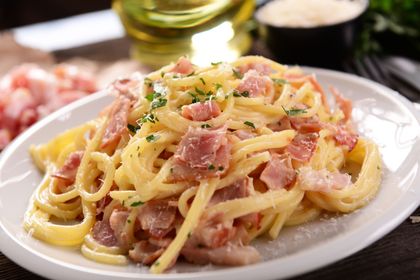 Pasta carbonara con tocino y queso parmesano en un plato blanco.