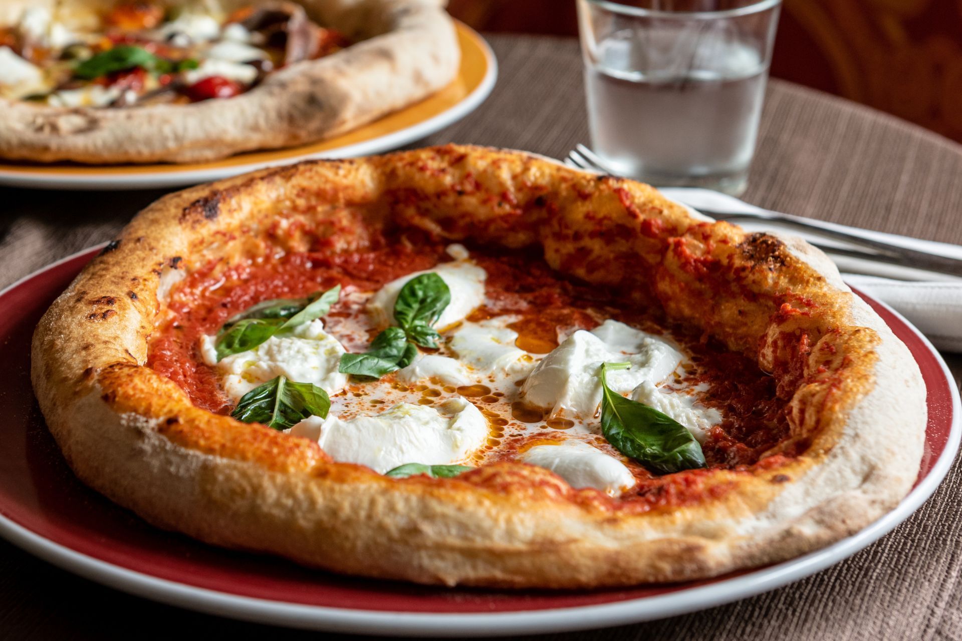 Pizza con masa gruesa, salsa de tomate, mozzarella, albahaca y aceite de oliva en un plato rojo.