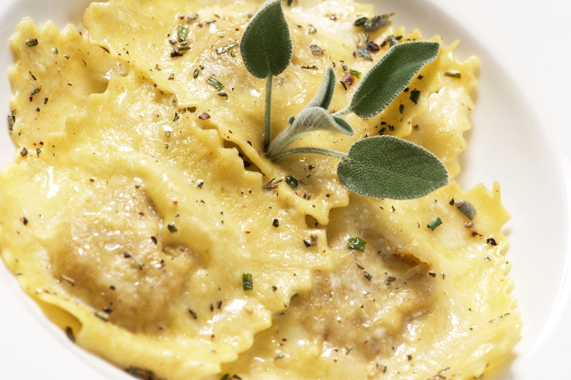 Raviolis con salvia y hierbas en un bol blanco.