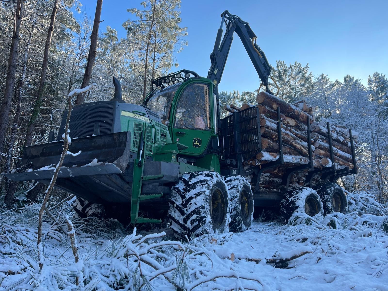 Camion forestier vert avec grue transportant des grumes coupées à travers une forêt enneigée