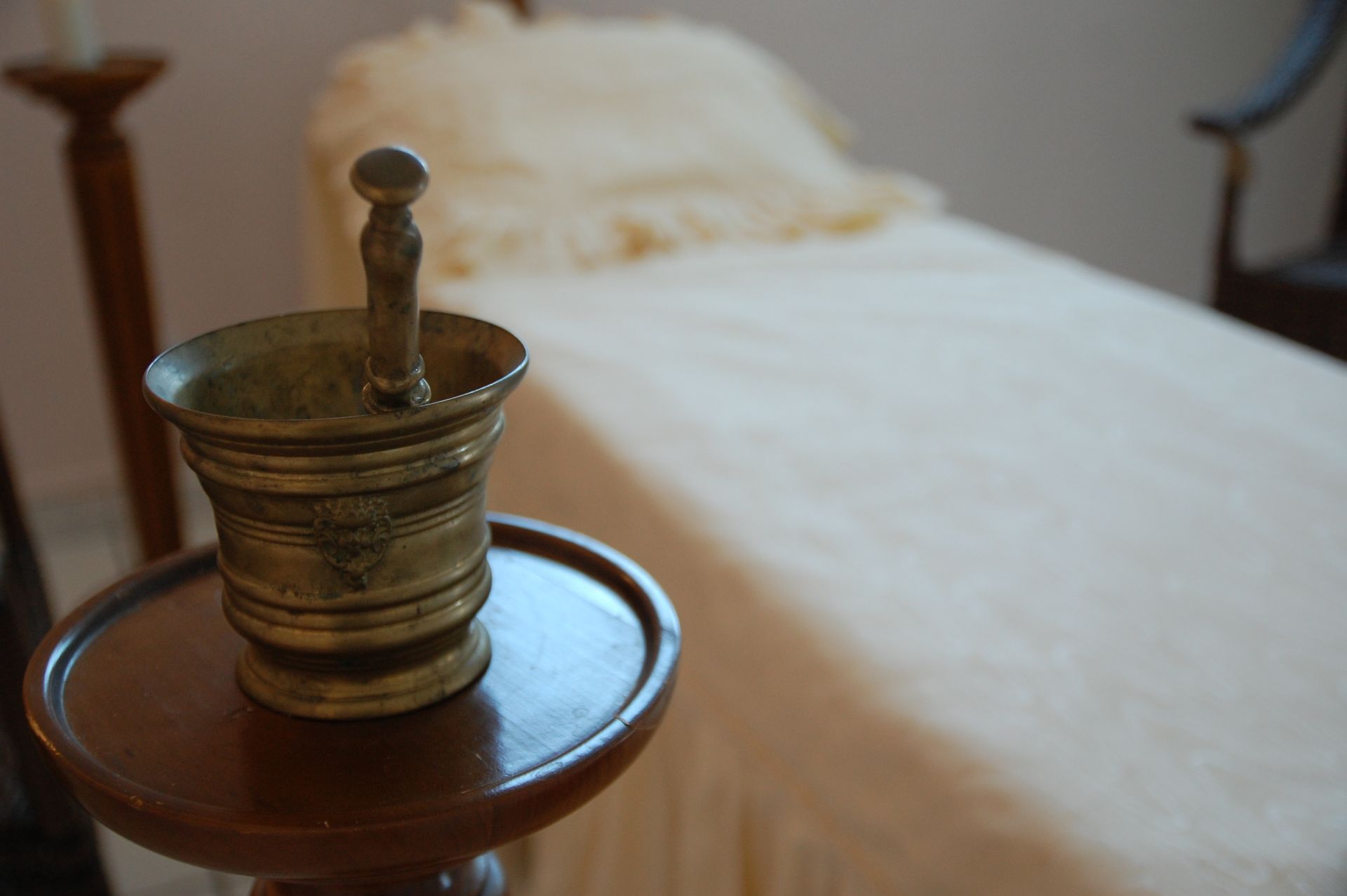 Mortier et pilon en laiton sur une petite table, lit en arrière-plan.