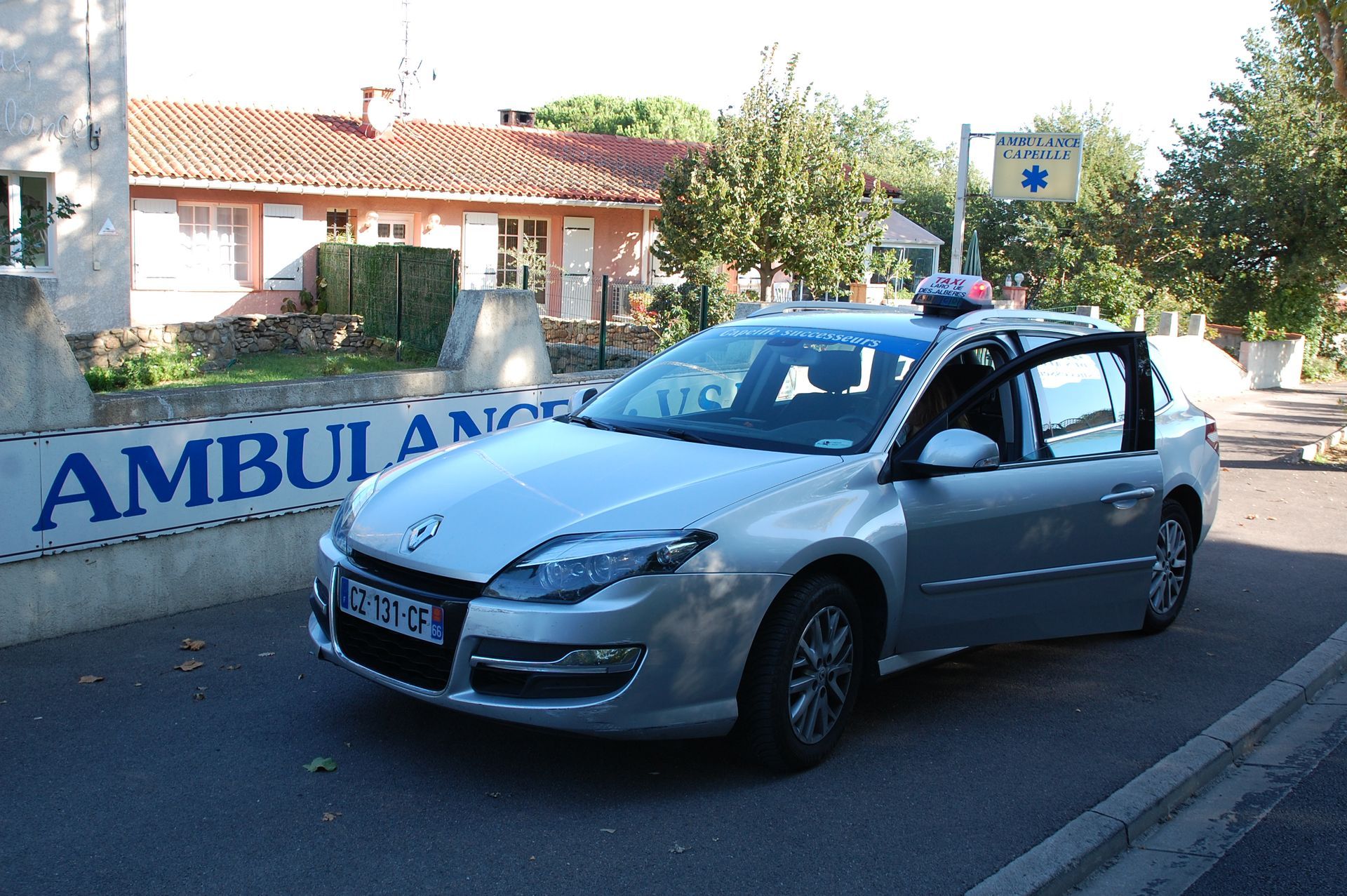 Une ambulance argentée est garée devant un bâtiment portant un panneau ambulance.