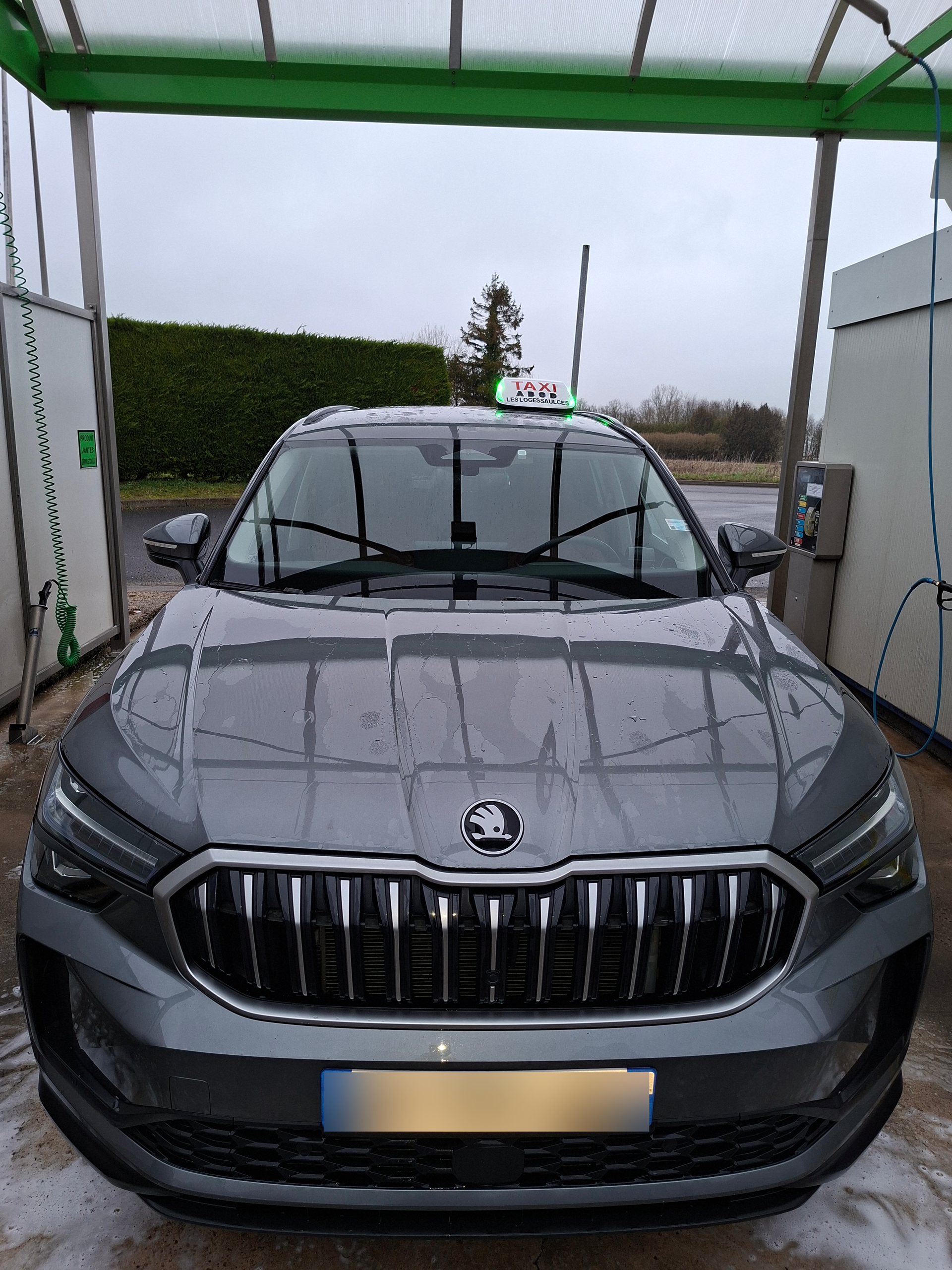 SUV Skoda gris dans une station de lavage, capot couvert de savon.