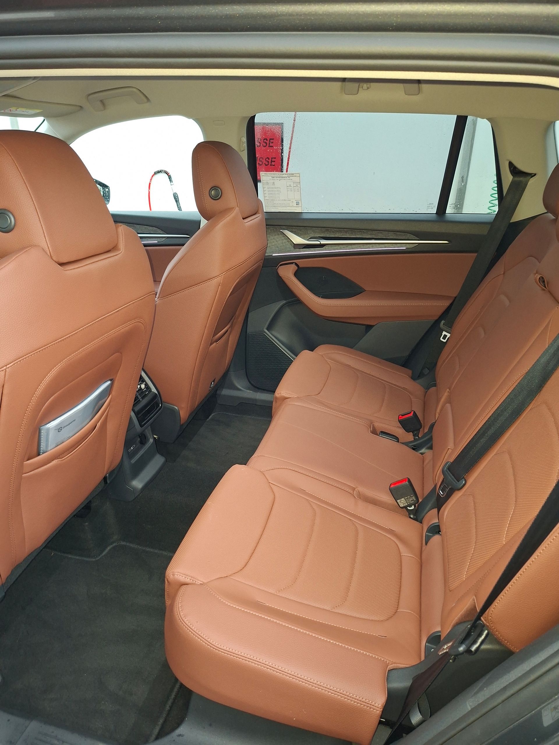 Intérieur arrière d'une voiture avec sièges en cuir beige. On aperçoit la banquette arrière, les appuie-têtes et le panneau de porte.