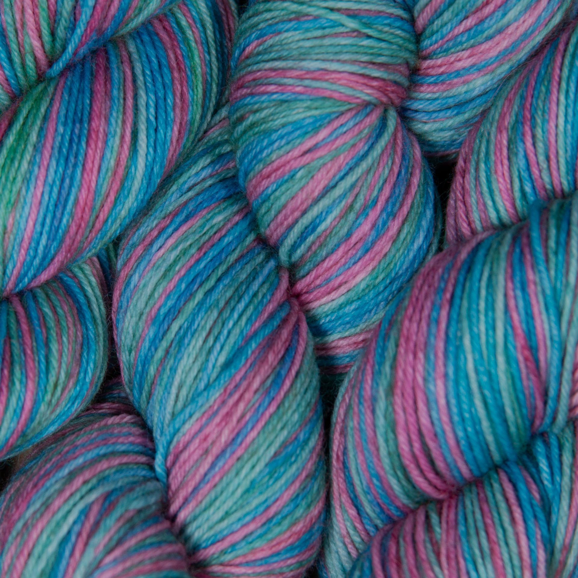 Knäuel aus buntem Garn in Türkis-, Rosa- und Grüntönen.