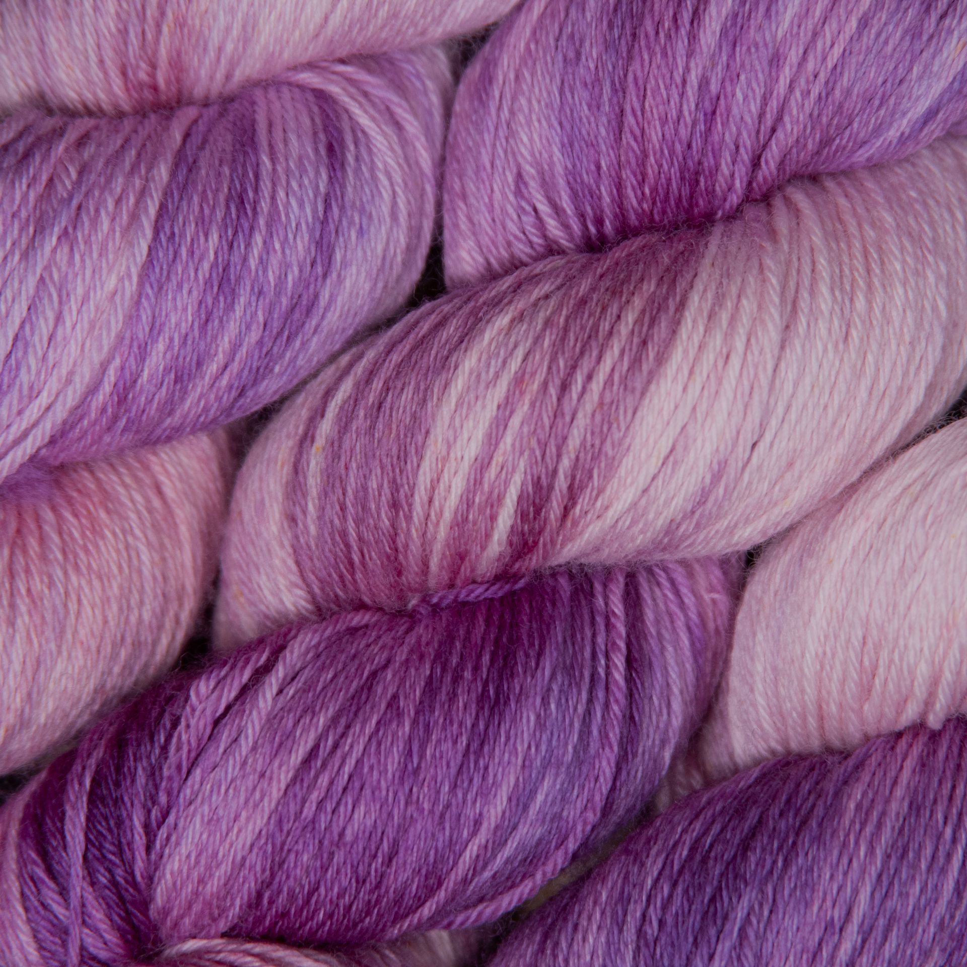 Nahaufnahme von Strängen handgefärbter Wolle in Rosa-, Lila- und Lavendeltönen.