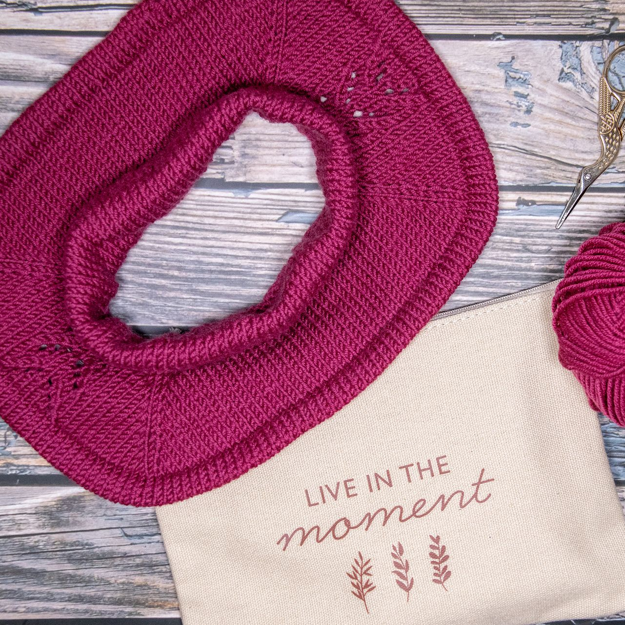 Gestrickter magentafarbener Schalkragen und eine Tragetasche mit der Aufschrift „Lebe im Moment“.