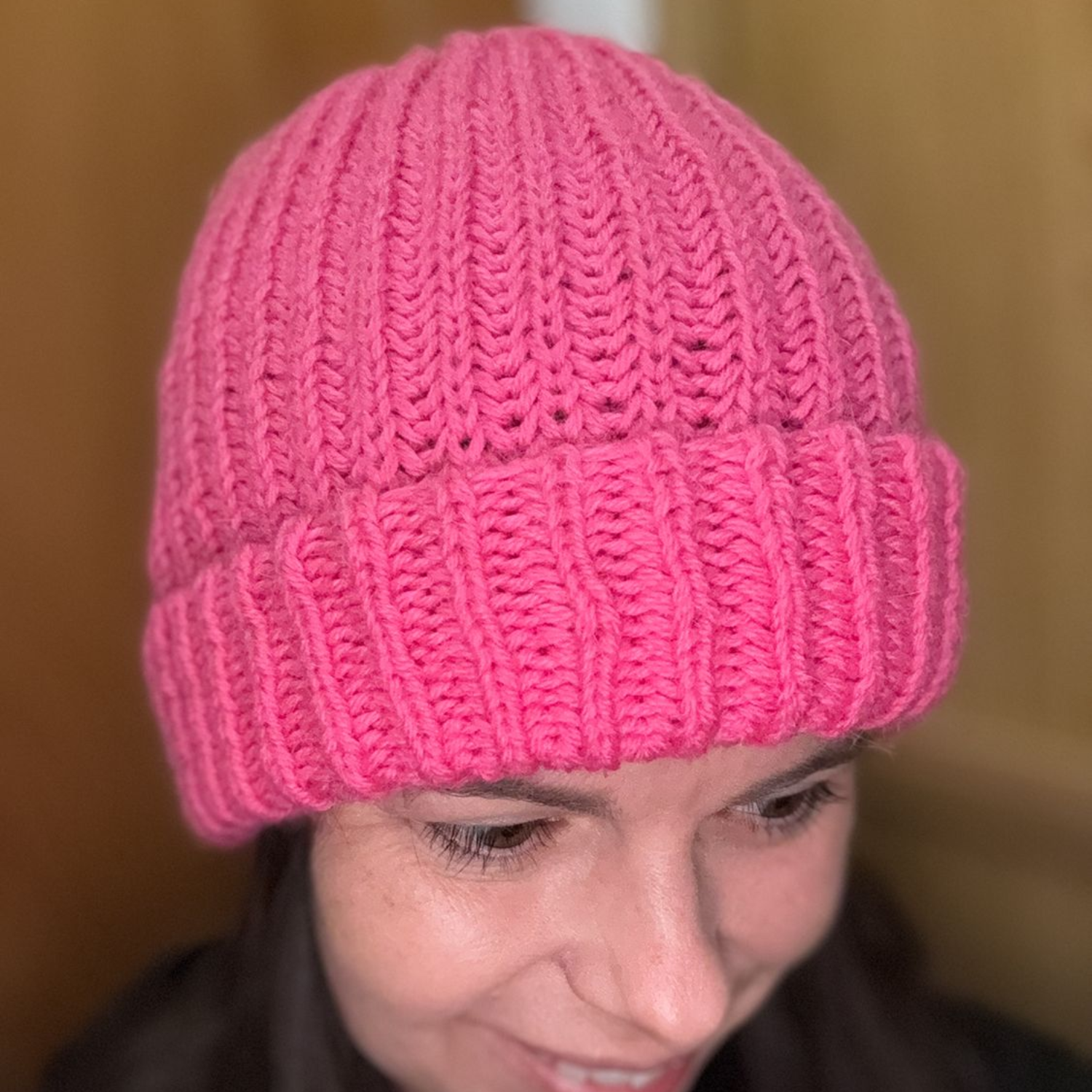 Strickzubehör: Wollknäuel, Stricknadeln, Schere, Maschenmarkierer, Stecknadel und eine Nadel auf einer Holzunterlage.