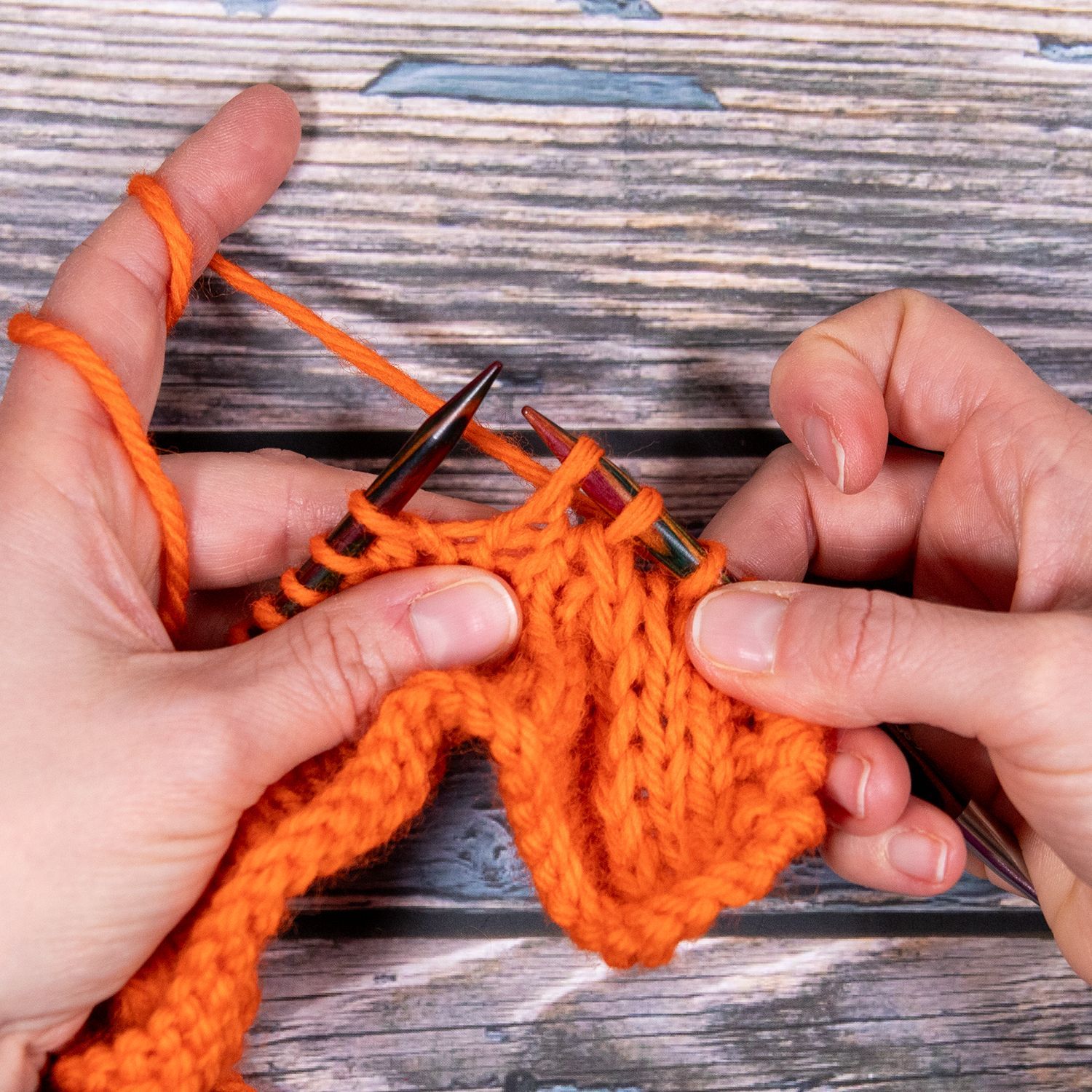 Hände stricken orangefarbenes Garn auf einer Holzoberfläche.