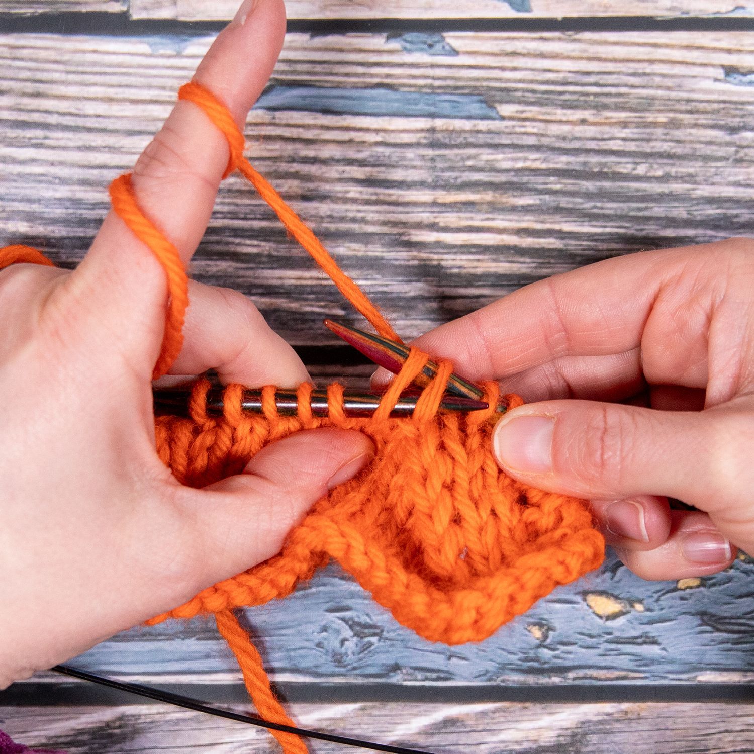 Hände stricken mit orangefarbenem Garn, Nahaufnahme.