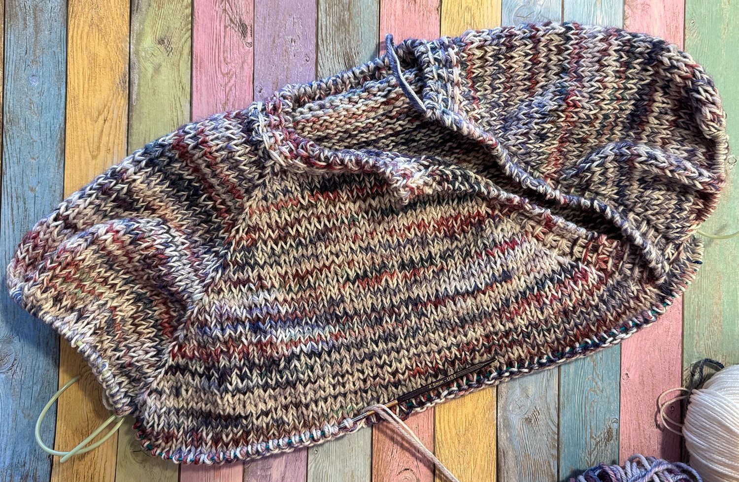 Gestrickter, mehrfarbiger Stoff liegt auf einer verwitterten Holzoberfläche mit Farbfeldern.