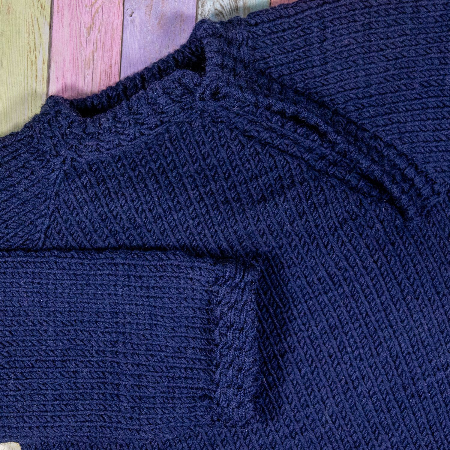 Dunkelblauer Strickpullover mit gerippten Bündchen und Kragen auf farbenfrohem Holzgrund.