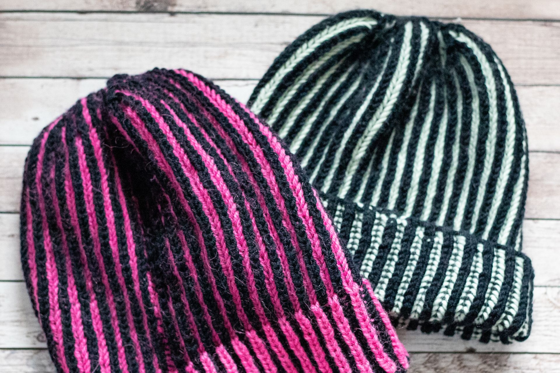 Gestrickter Rippenstoff aus grauem Garn auf Holzunterlage, mit Wollknäueln und Stricknadeln.