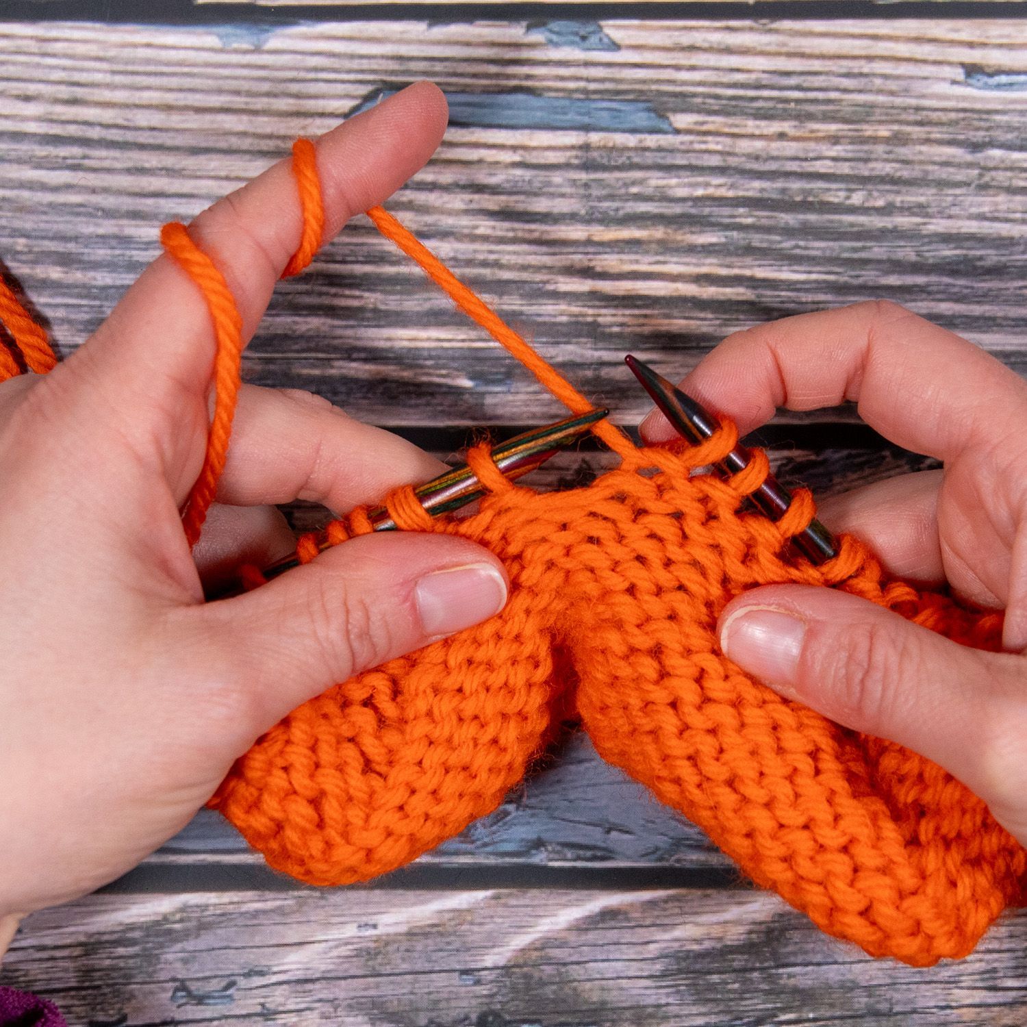 Hände stricken mit orangefarbenem Garn. Nahaufnahme von Nadeln und dem entstehenden Strickstück.