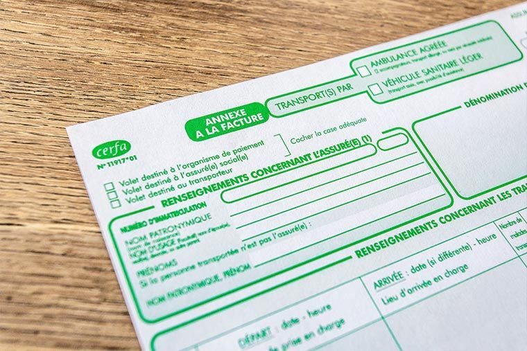 Gros plan sur un formulaire français de transport médical, avec texte vert sur fond blanc, posé sur une surface en bois.