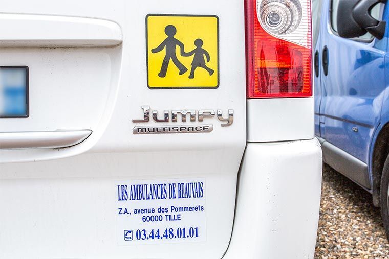 Fourgonnette blanche avec un panneau de passage piéton scolaire, le logo « Jumpy » et les informations « Les Ambulances Du Tillois ».