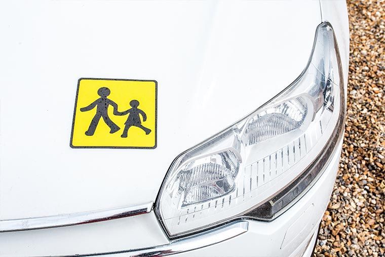 Capot de voiture blanc avec un panneau de passage piéton jaune à côté d'un phare.