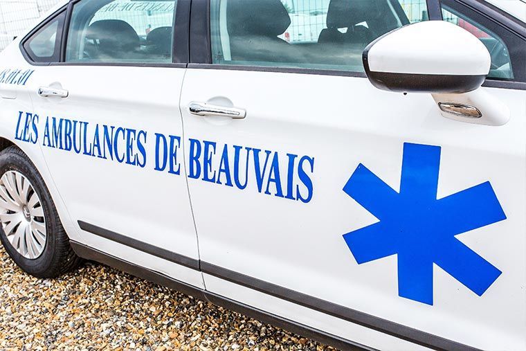 Ambulance blanche avec l'inscription bleue « LES AMBULANCES DE BEAUVAIS » et une étoile de vie bleue.