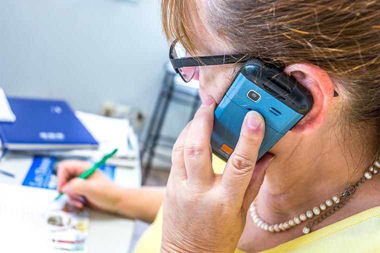 Femme au téléphone, écrivant à son bureau. Téléphone bleu à l'oreille, stylo à la main, regard baissé.