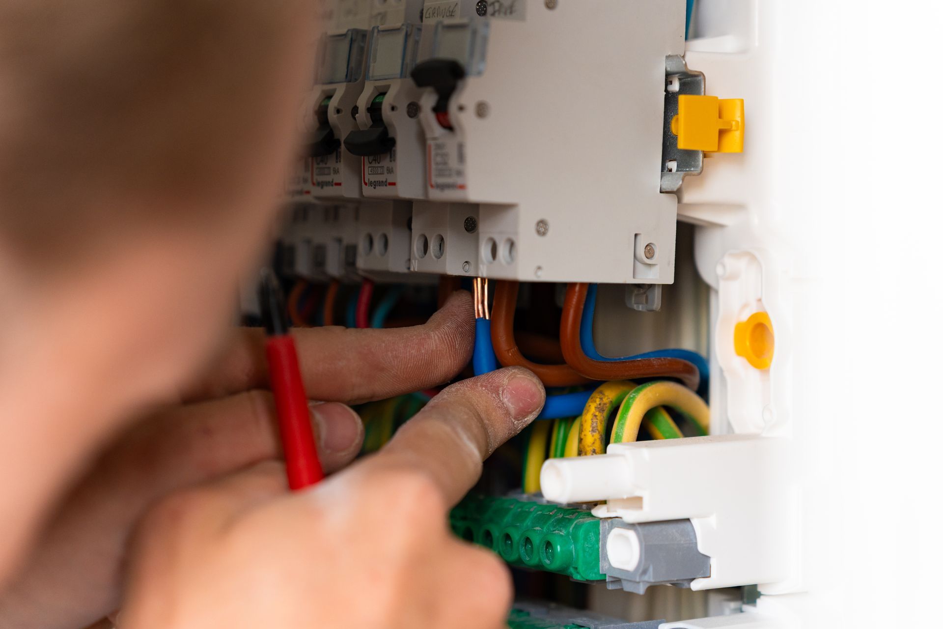 Les mains d'un électricien travaillant sur un tableau électrique, tenant une sonde rouge et touchant des fils.
