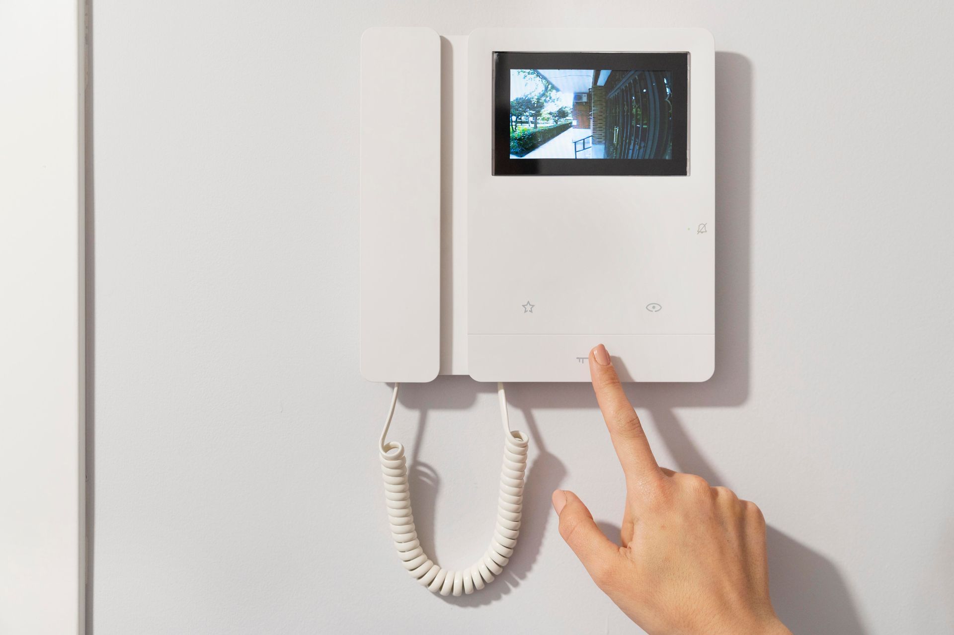 Doigt touchant un visiophone mural connecté à l'interphone du portail électrique d'une maison
