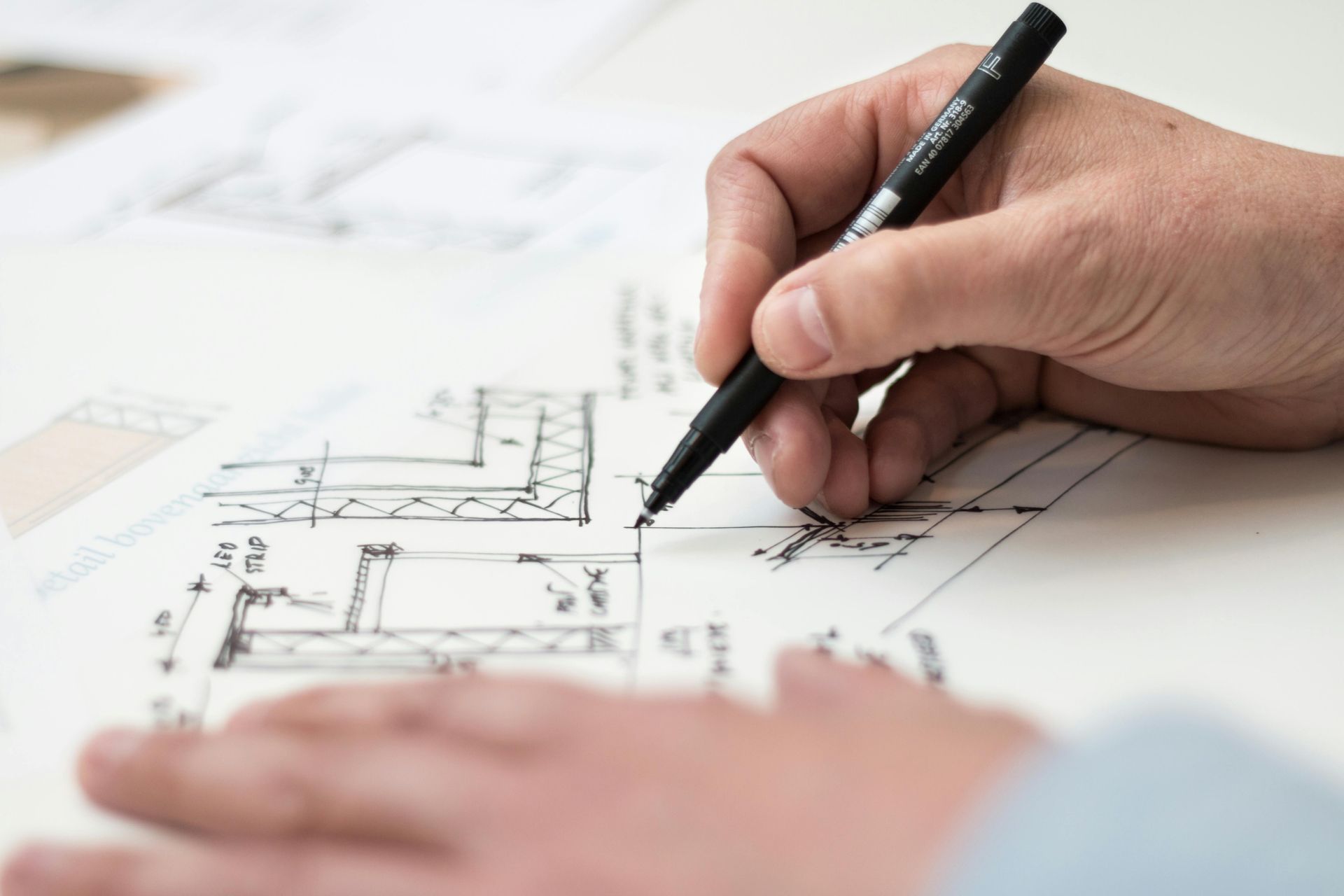Main tenant un stylo noir et dessinant un plan technique en vue de travaux
